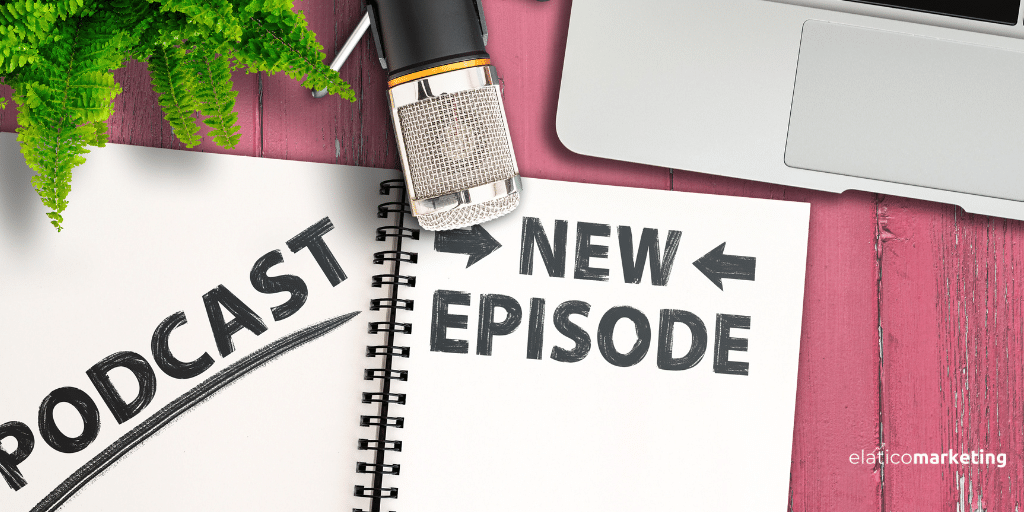 Mesa de color rosa con una libreta en la que está escrito Podcast, New Episode. Además, hay un micrófono y un ordenador portátil sobre la mesa, indicando las herramientas para el podcast.